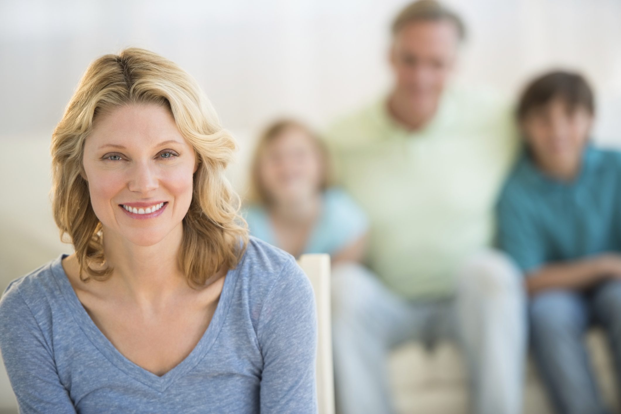 Woman With Family Sitting On Sofa In Background At Home